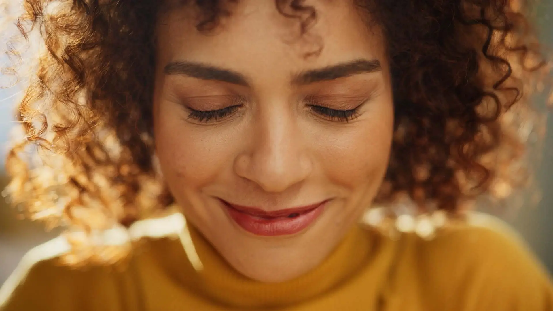 Close-up of a smiling woman with curly hair and natural lighting, representing creativity, confidence, and authenticity in our marketing and web design approach.